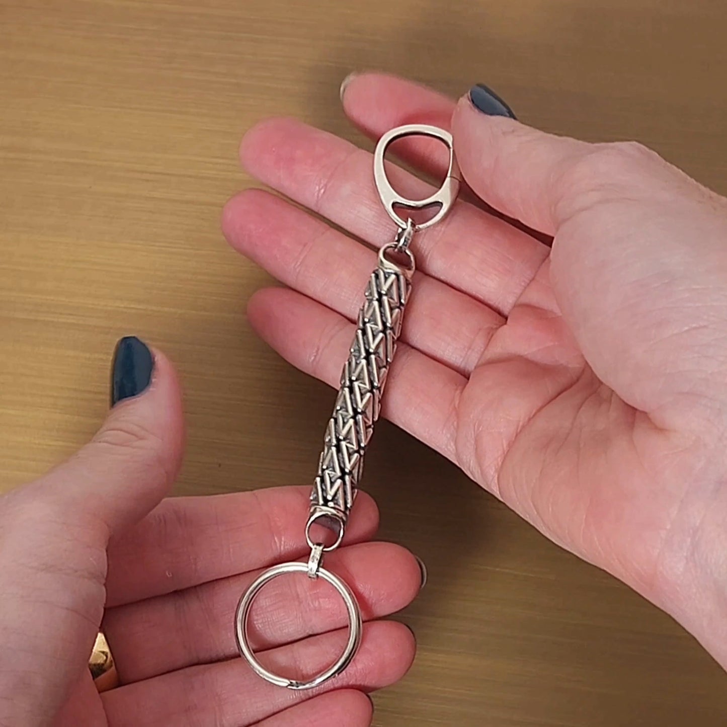 Geometric sterling silver designer keychain with precise dimensional details presented by female hands.