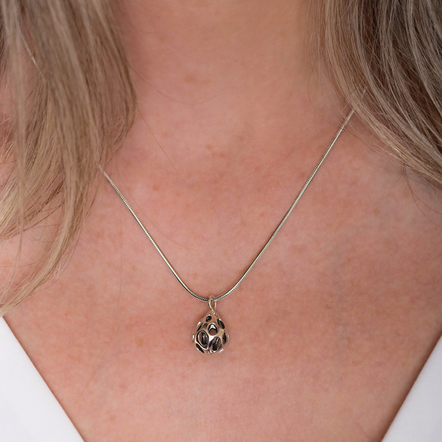 Xover0’s sterling silver OLEA pendant necklace worn at the center of a V-neck décolleté. The dimensional teardrop design catches the light, highlighting its sculptural form and polished finish.