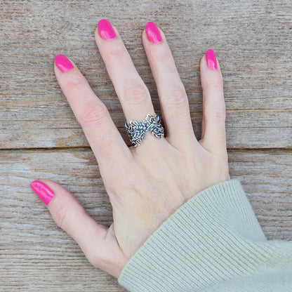 Hand with pink nail polish wearing a sterling silver calligraphic ring on a wooden surface